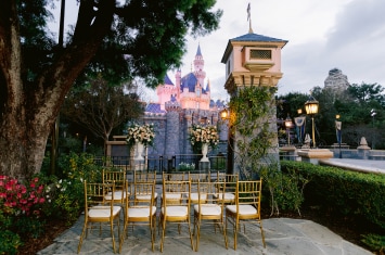 Wedding chairs and floral arrangements set up for a wedding ceremony in front of the illuminated Sleeping Beauty Castle at Disneyland