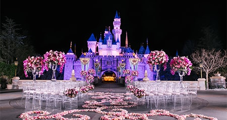 An evening ceremony setup with chairs, floral arrangements and Sleeping Beauty Castle illuminated in the background