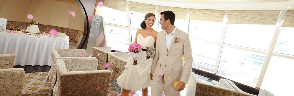 Flower petals fall through the air while a bride and groom walk through their reception hall