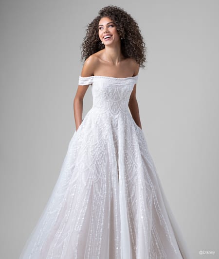 The front of a bride wearing a Jasmine inspired A line gown featuring beading and an off the shoulder neckline