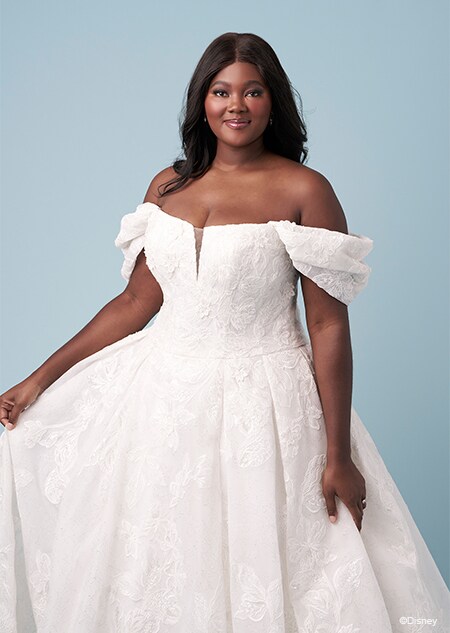 A bride wearing an Aurora inspired A line wedding gown featuring embroidery, an illusion neckline and off the shoulder sleeves