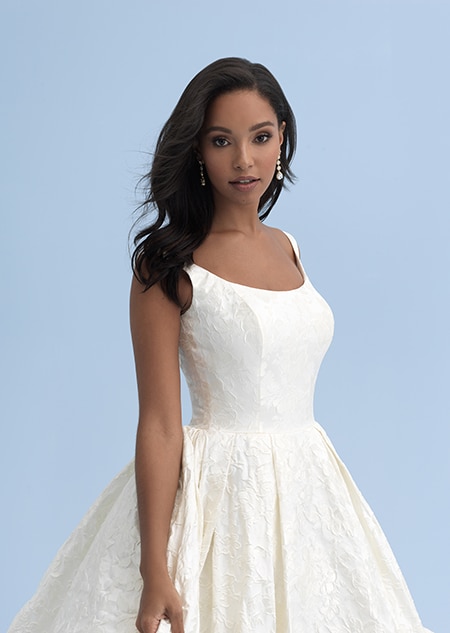 A close up of a woman with shoulder length hair wearing long earrings and a wedding dress with thick straps across her shoulders