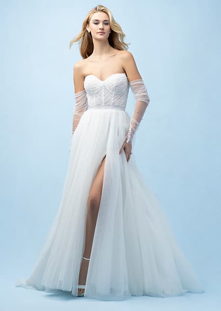 The front of a bride wearing an Ariel inspired A line gown featuring a sweetheart neckline, lightly beaded fabric, a high slit in the skirt and sheer lower arm wraps