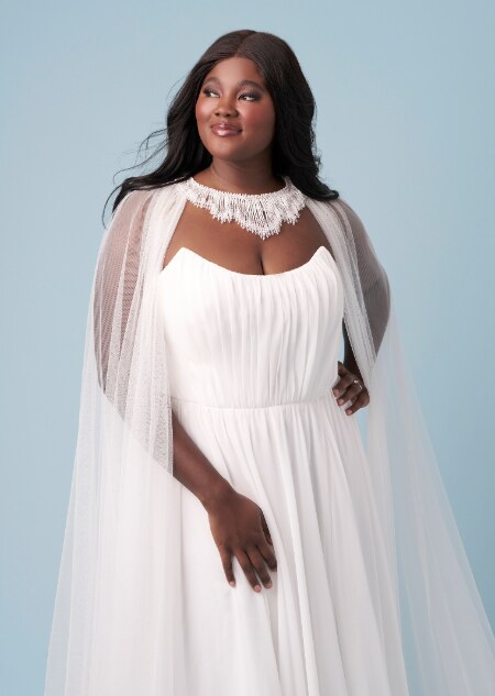 A bride wearing a strapless Jasmine inspired sheath gown featuring a scoop neckline and a sheer cape