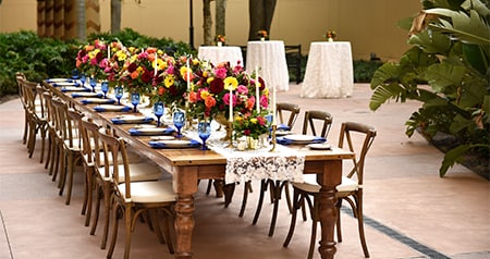 An outdoor dining setup with a wooden table and chairs, decorated with floral centerpieces, glassware and table settings