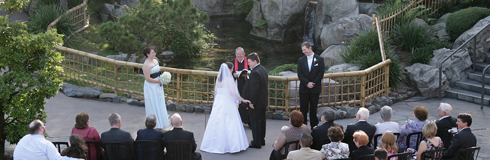 A couple marries in front of a koi pond with a priest and Guests watching