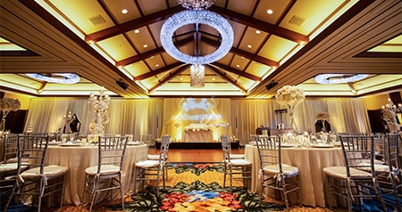 Several tables with place settings and a dance floor in the Kaiona Ballroom decorated with large bouquets of flowers