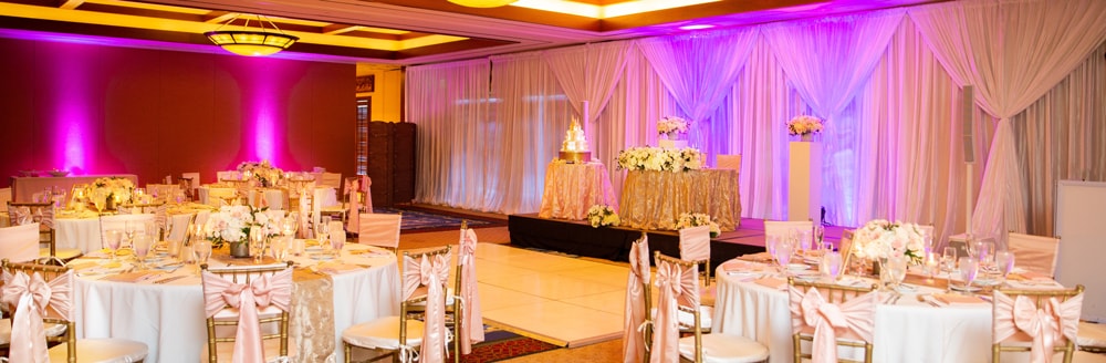 A dance floor in the middle of a reception hall holding several round tables and a cake table