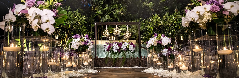 Several lit candles line an aisle along with several bouquets of flowers