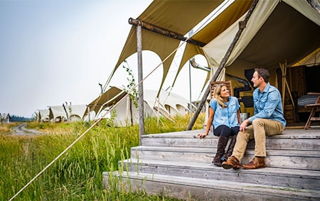 Smiling newlyweds in front of a tent under blue skies in Yellowstone National Park