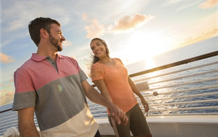 A man and a woman hold hands while strolling along the deck of a Disney Cruise Line ship
