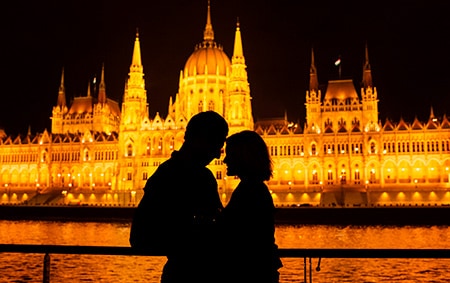 A silhouette of a man and a woman at night in front of a castle lit up by lights