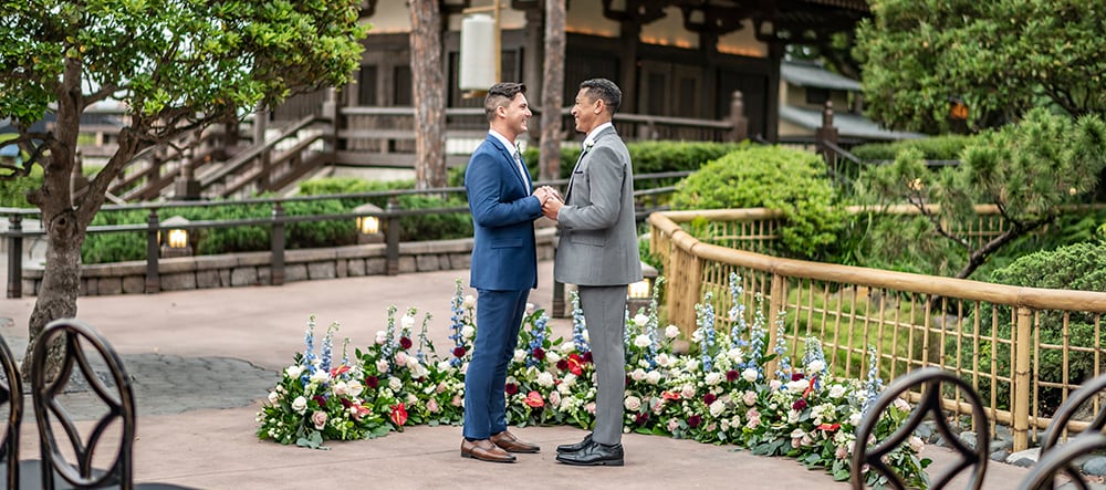 Two men are all smiles as they hold hands and look into each other’s eyes near a bamboo fence in the EPCOT Japan Pavilion at Walt Disney World Resort