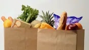 Alaska Two packed bags of groceries, with apples, celery, a baguette and other food showing