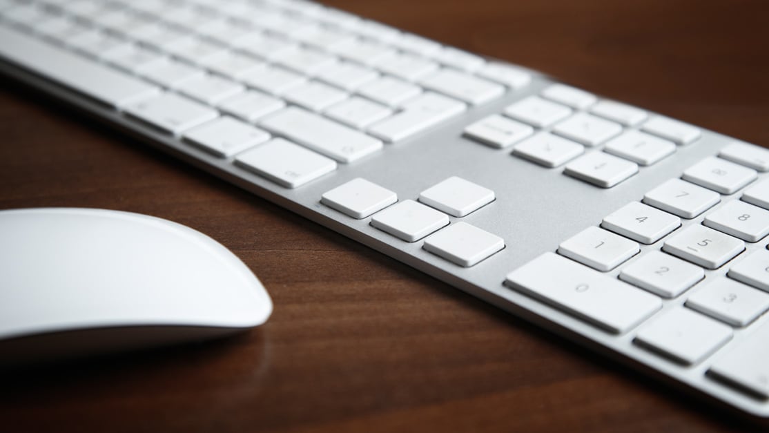 A keyboard and mouse atop a wood table