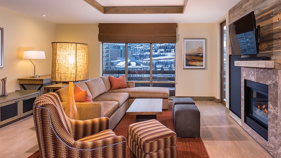 A living room area with a sofa, coffee table, lamp, framed art on the wall and a fireplace