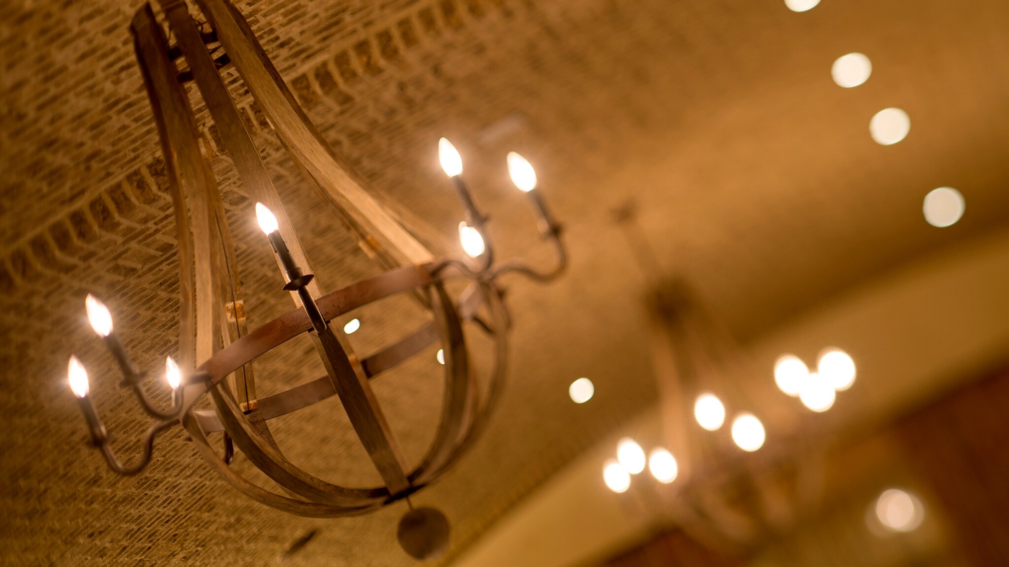 A dining room with tables, chairs, chandeliers and a rounded brick ceiling