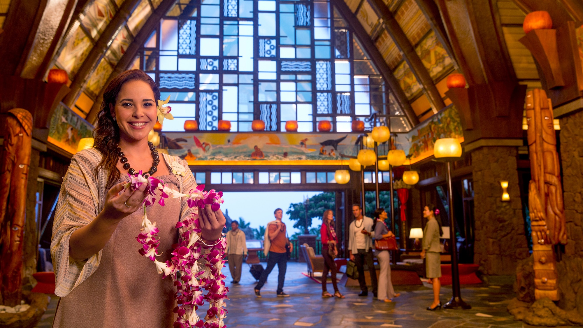 A female Cast Member standing in the Aulani Resort lobby, welcoming new Guests with lei necklaces