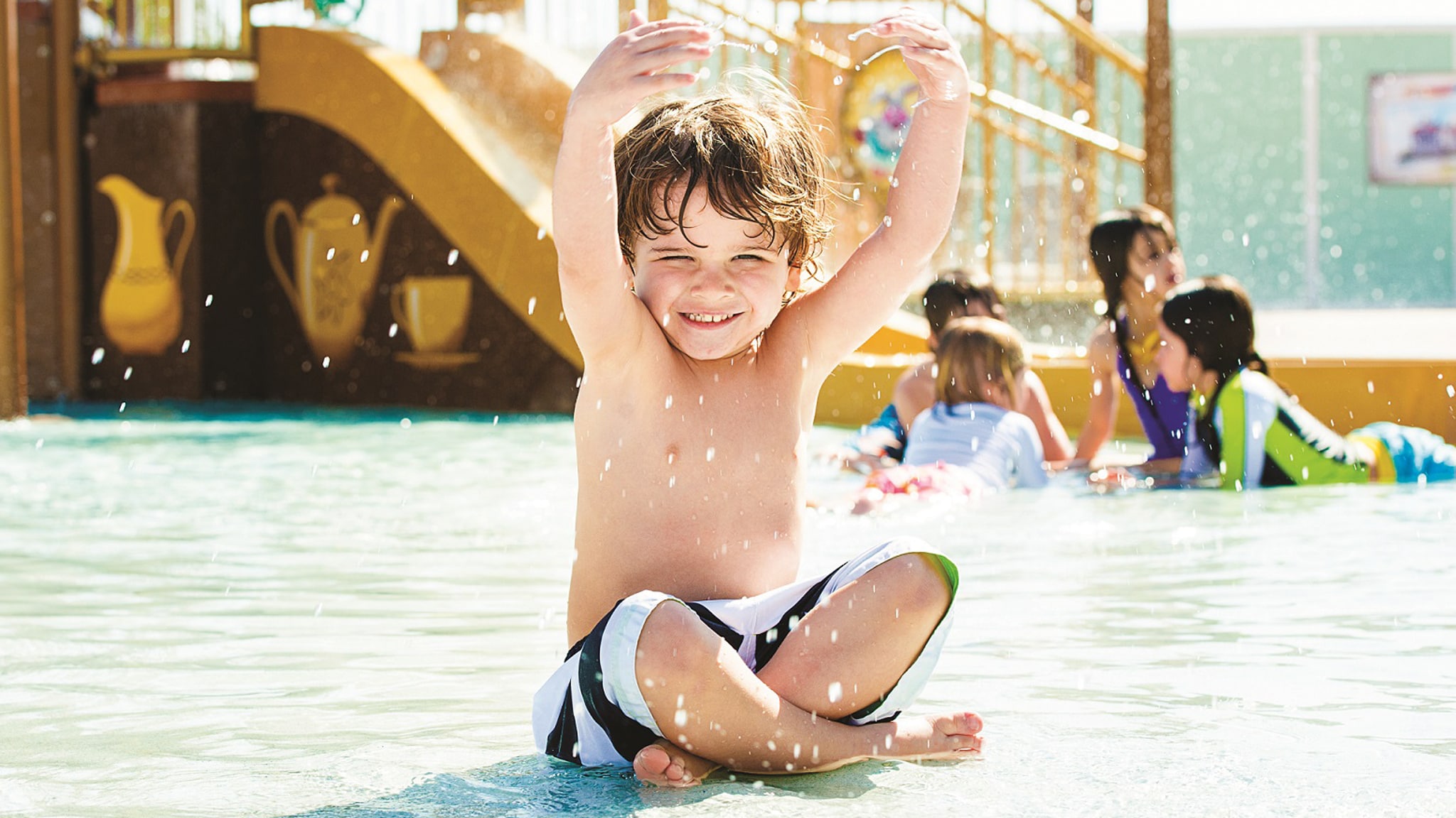 A young boy smiling while sitting in a splash play area at a Resort pool