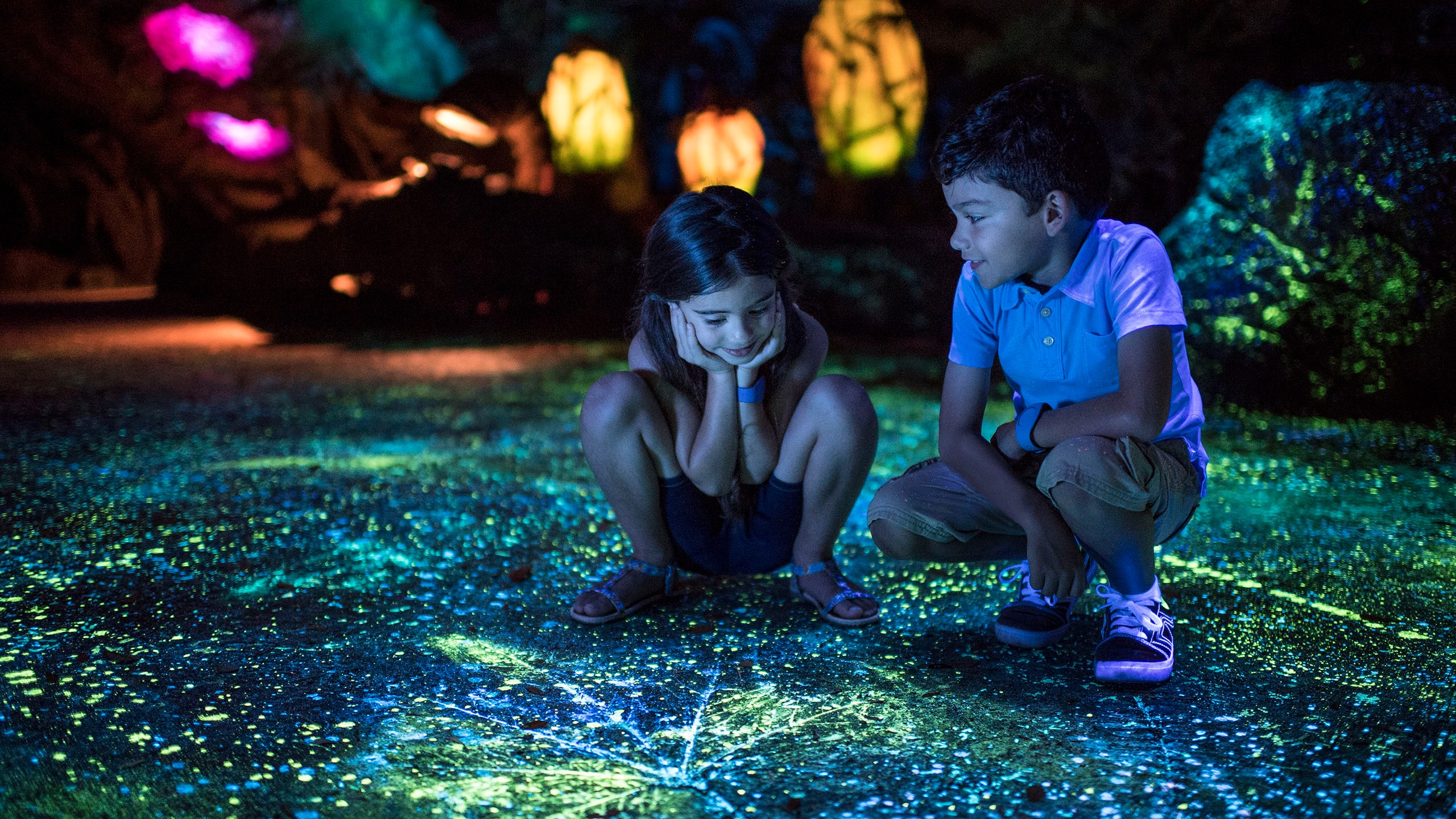 A boy and a girl crouching in a bioluminescent cavern