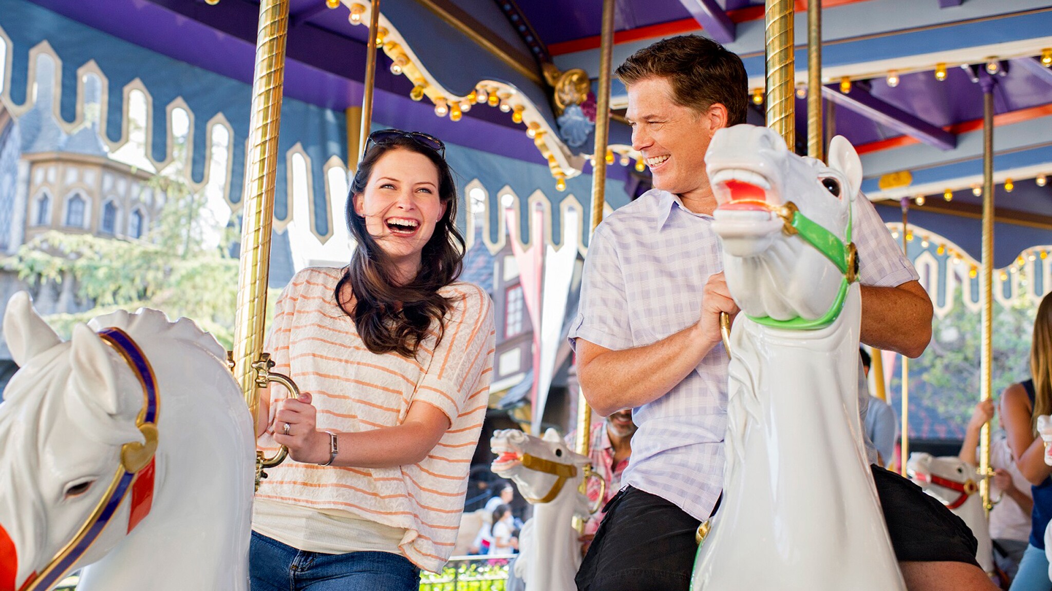 A man and woman riding on carrousel horses side-by-side