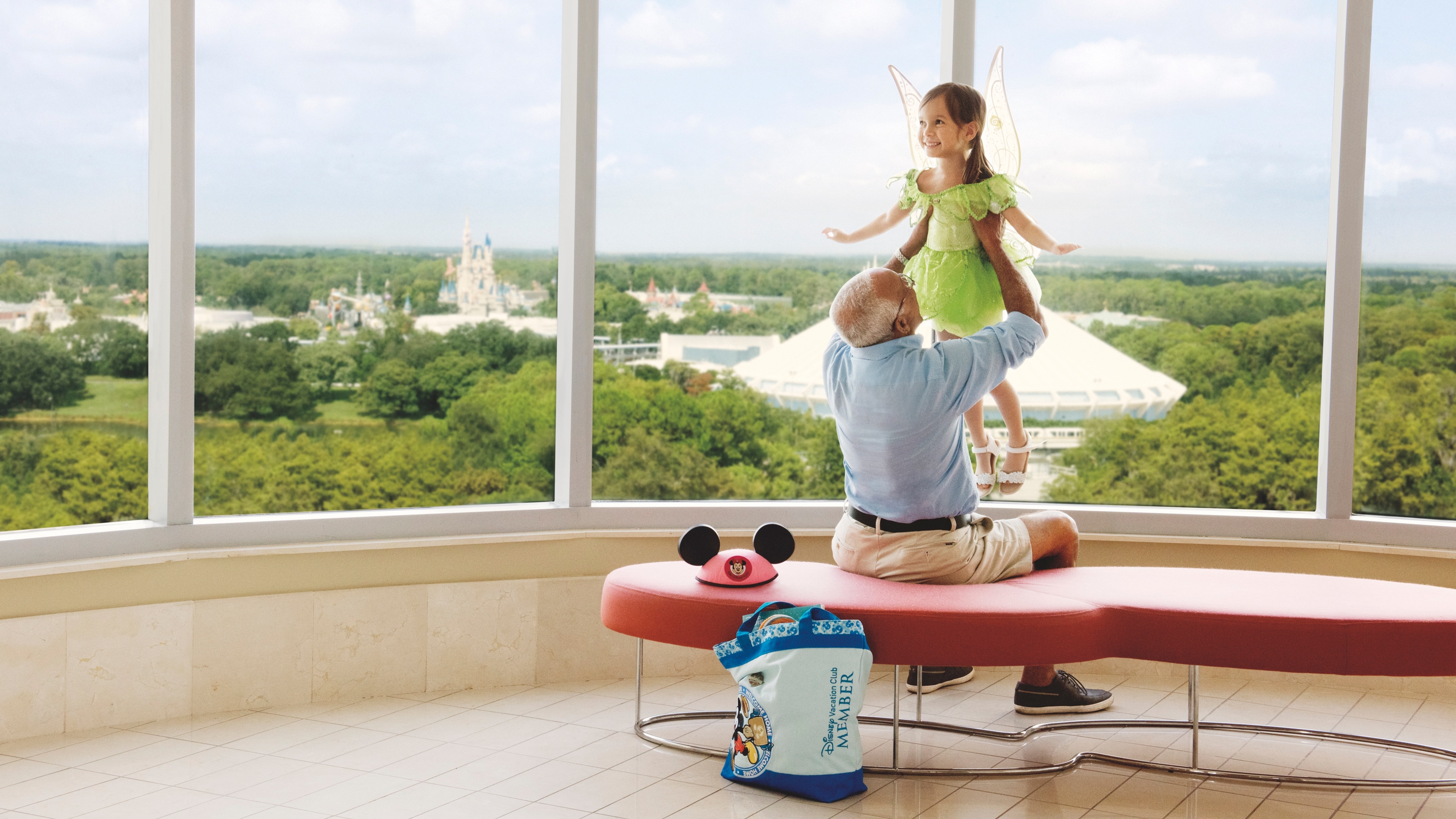 A man lifts his granddaughter near a window facing Cinderella Castle
