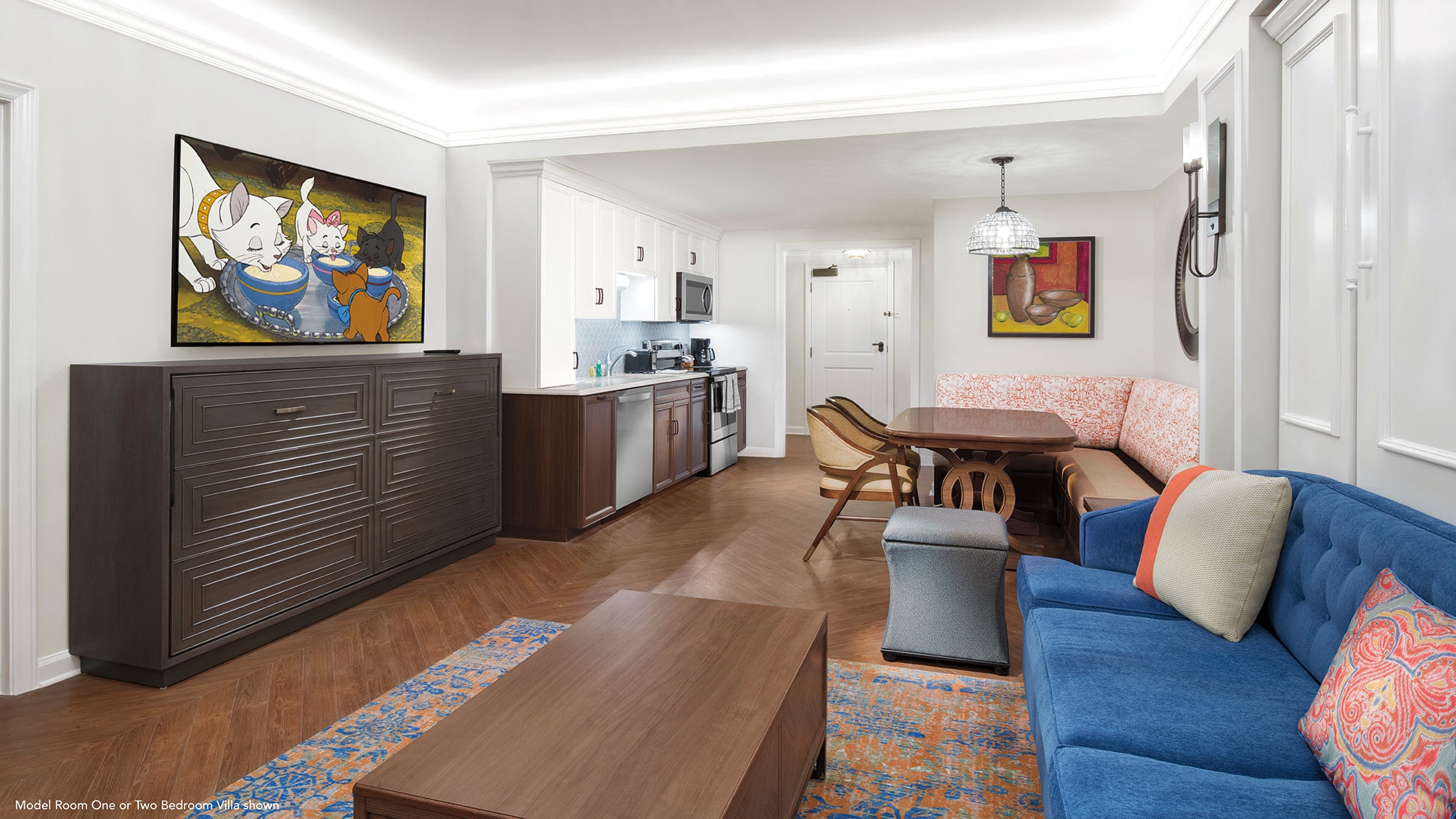 A long room with a kitchen, dining room, and living room with a couch, coffee table and flat-panel TV