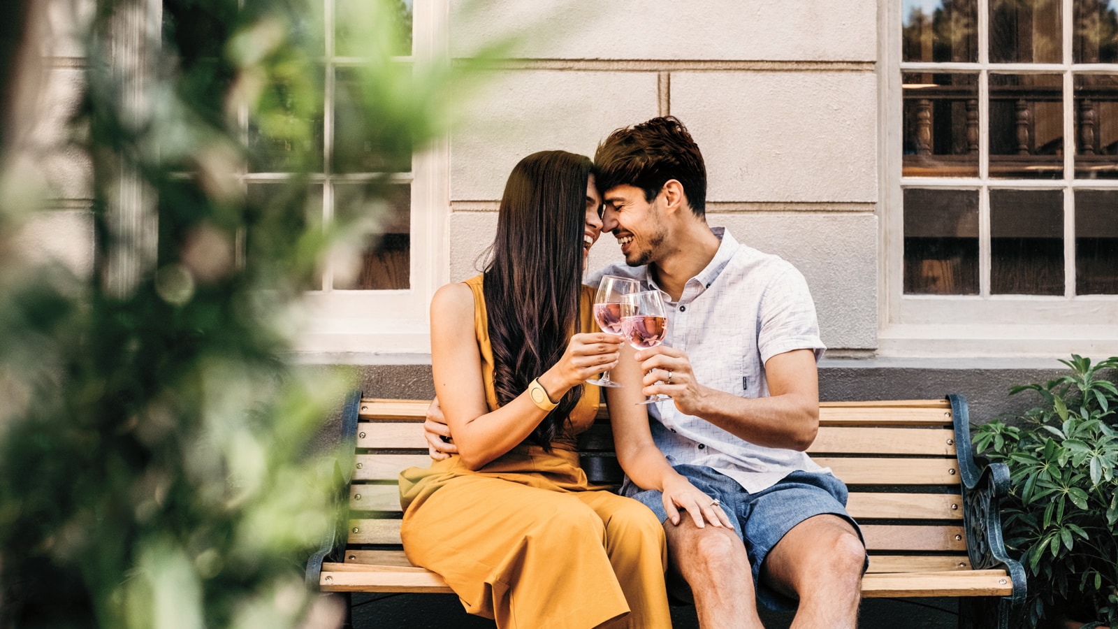 A couple embraces on a bench as they toast with wine
