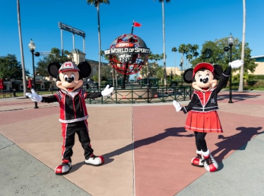 Minnie Mouse and Mickey Mouse standing near the ESPN Wide World of Sports Complex globe while dressed in sports themed attire