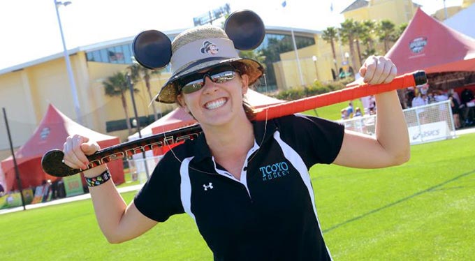 Home Slide - Lacrosse A field hockey player wearing a Mickey Ears straw hat relaxes with her stick on her shoulder