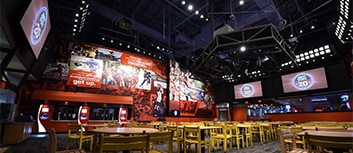 Tables and chairs fill the floor of a room witzh large TVs and a sports mural hanging on the walls at ESPN Wide World of Sports Grill